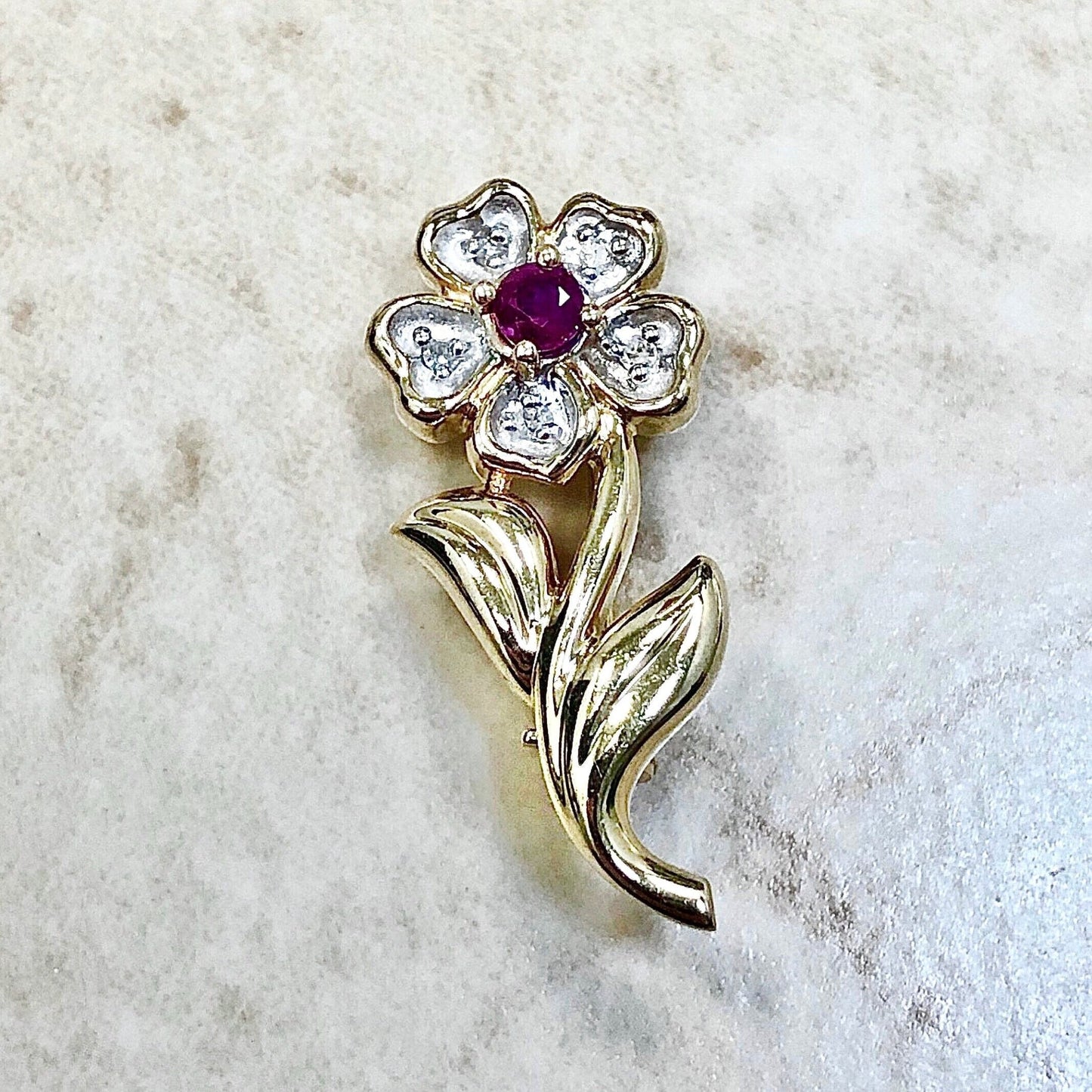 A lovely brooch crafted in 14 karat yellow gold set in the center with a round ruby. It is haloed with 5 round diamonds. The brooch was designed as a flower.